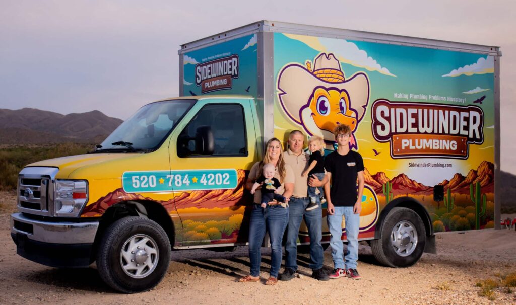 Family of five posing in front of a colorful Sidewinder Plumbing truck in a desert setting at dusk/late afternoon.